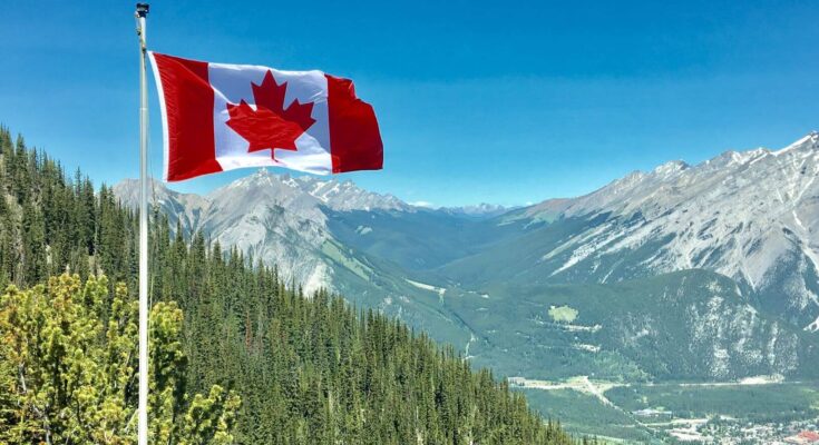 An image of the Canadian flag flying high over a scenic mountain landscape.